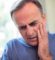 A mature Man grimacing and rubbing his cheek due to a toothache